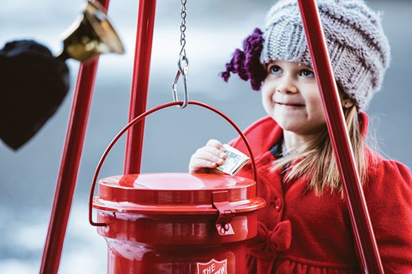 A young girl in a winter coat prepares to donate money to a Salvation Army red kettle.