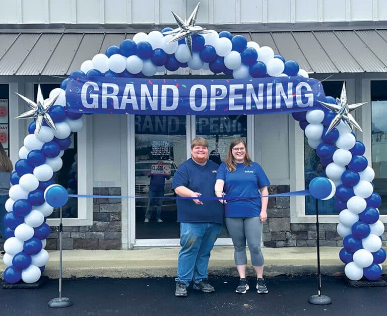 Nick and Sarah Burtram, owners of Buddy Bins, located at 105 Sutton Bridge Road in Rainbow City, cut a blue ribbon in front of a blue and white balloon arch on the business' opening day.