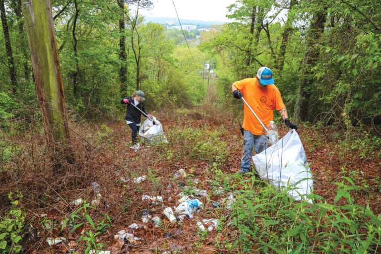 Two people pick up trash in a forest background in Gadsden.