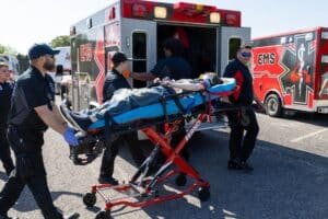 Emergency responders transport a person on a stretcher toward an ambulance.